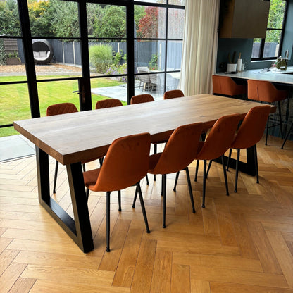 Long wooden dining table with orange chairs in a modern kitchen setting.