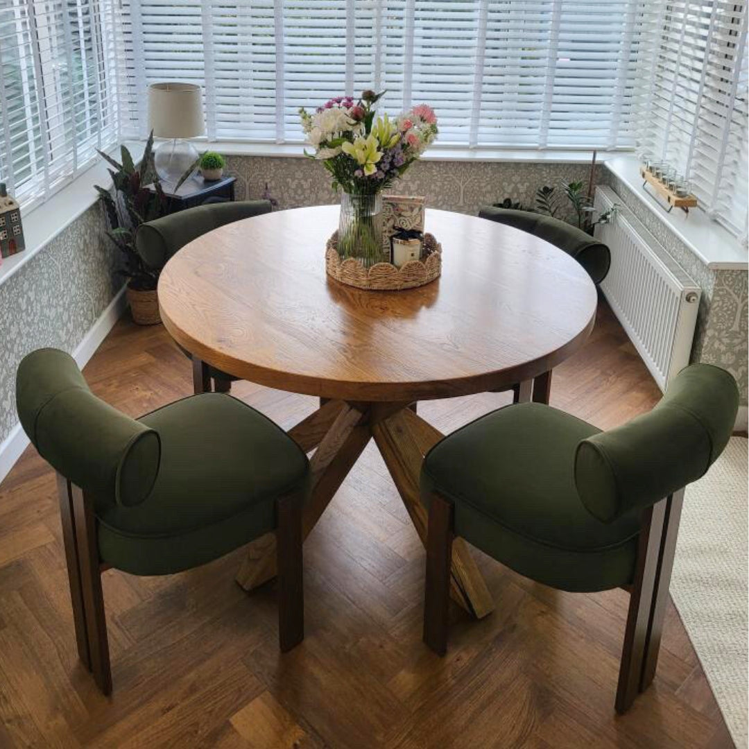 Round wooden dining table with four green chairs in a room with large windows.