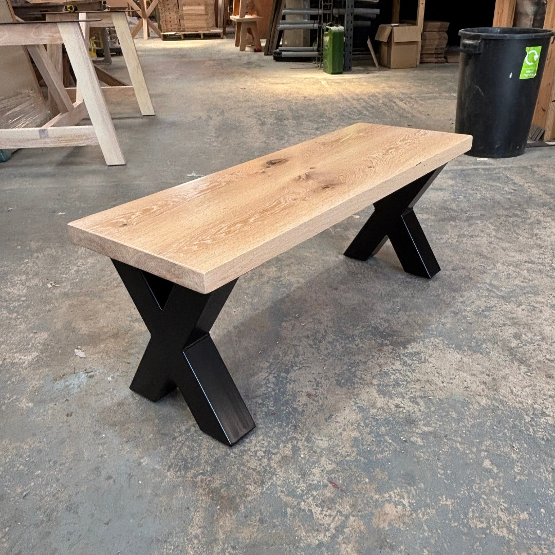 Wooden bench with black X-shaped legs on a concrete floor.