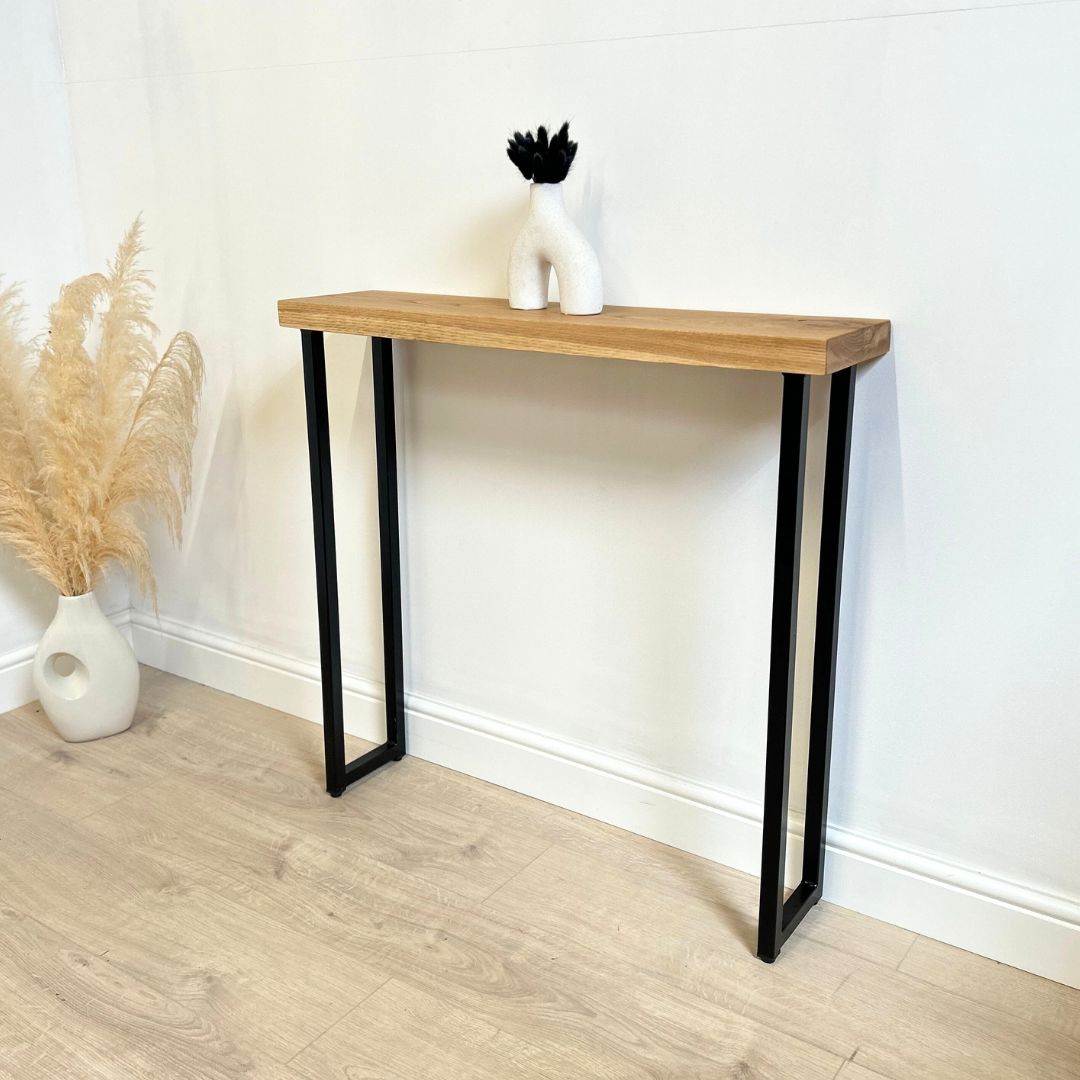 A modern oak entry table with a black powder coated steel exposed box frame. The table is set against a white background, and there are decorative items on top.